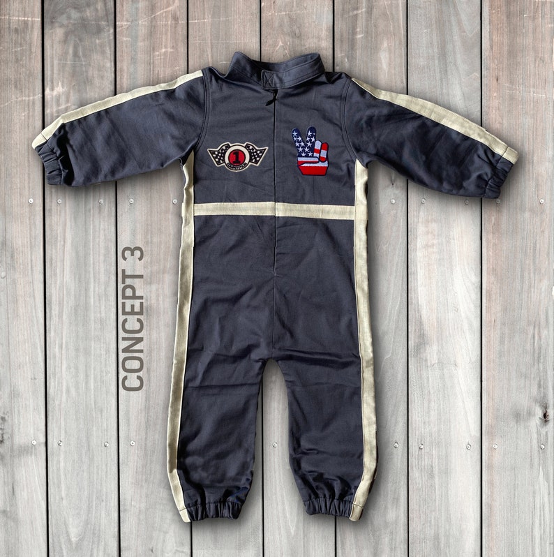 May include: A dark gray jumpsuit with white stripes down the sides. The jumpsuit has a patch on the chest with a number one and wings, and a peace sign patch with an American flag design on the right shoulder. The text "CONCEPT 3" is written vertically on the left side of the image.