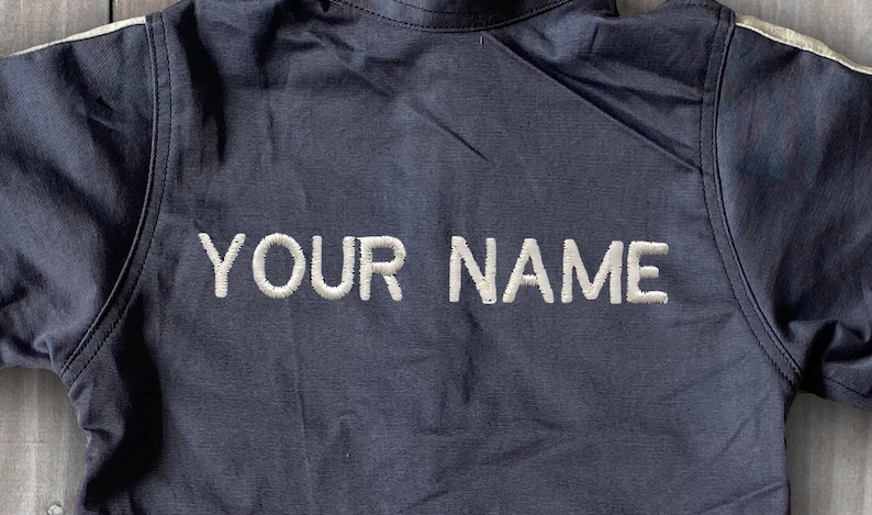 May include: A dark blue jacket with white piping on the sleeves and a white embroidered "YOUR NAME" on the back.