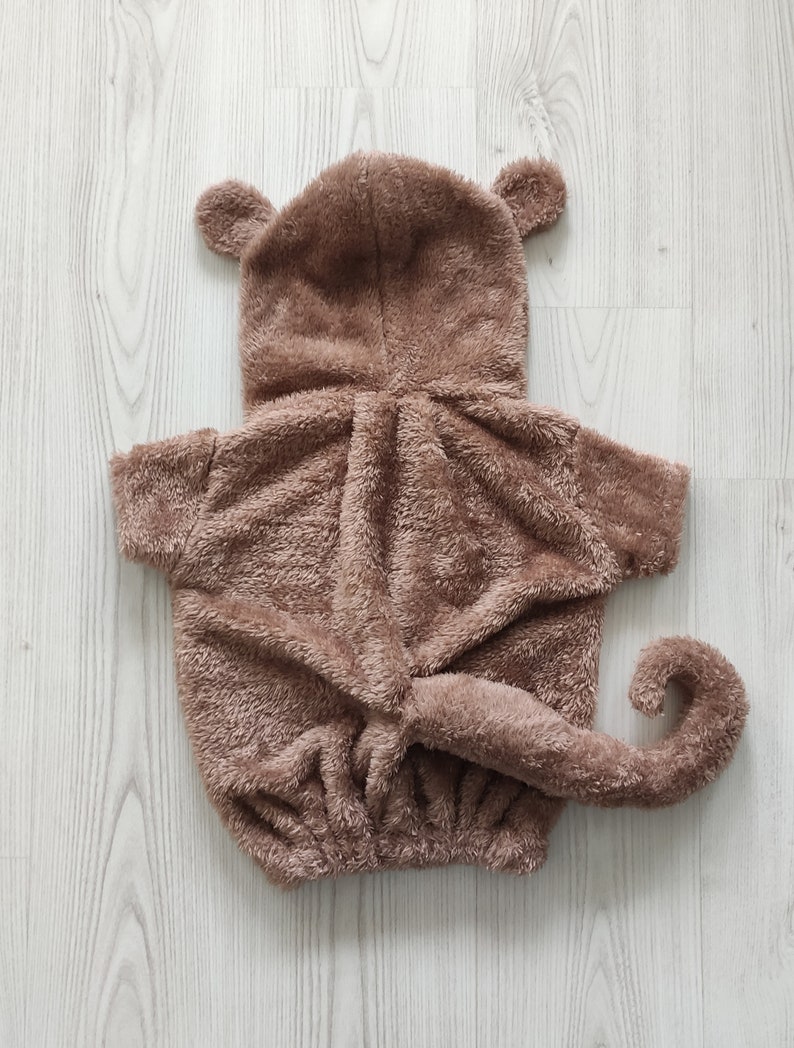 Puede incluir: Un disfraz de mono de peluche marr&oacute;n con capucha y cola. El disfraz est&aacute; hecho de tela suave y peluda y tiene un dise&ntilde;o lindo y juguet&oacute;n.