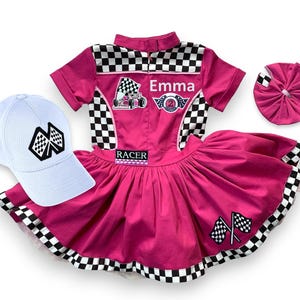 May include: A pink racing-themed outfit set with a matching white baseball cap. The set includes a collared shirt with checkered accents, a skirt, and a headband. The shirt has the name "Emma" and racing patches.
