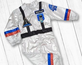Può includere: Un costume da astronauta argentato con bordi blu e rossi. Il costume ha delle toppe che dicono "Space Pilot" e "Space Explorer". Il nome "Michael" è scritto su una toppa sul petto.