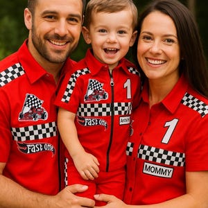 Könnte beinhalten: Eine dreiköpfige Familie trägt passende rote Hemden im Rennsport-Stil. Die Hemden zeigen ein kariertes Flaggen-Design, die Nummer "1" und die Wörter "Fast One" und "Mommy". Das Kind trägt einen Rennanzug.