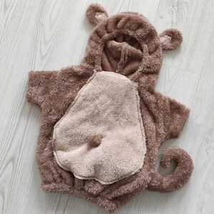 Puede incluir: Un disfraz de mono de peluche marr&oacute;n para un beb&eacute; o un ni&ntilde;o peque&ntilde;o. El disfraz tiene una capucha con orejas, una cola y un parche en el vientre.