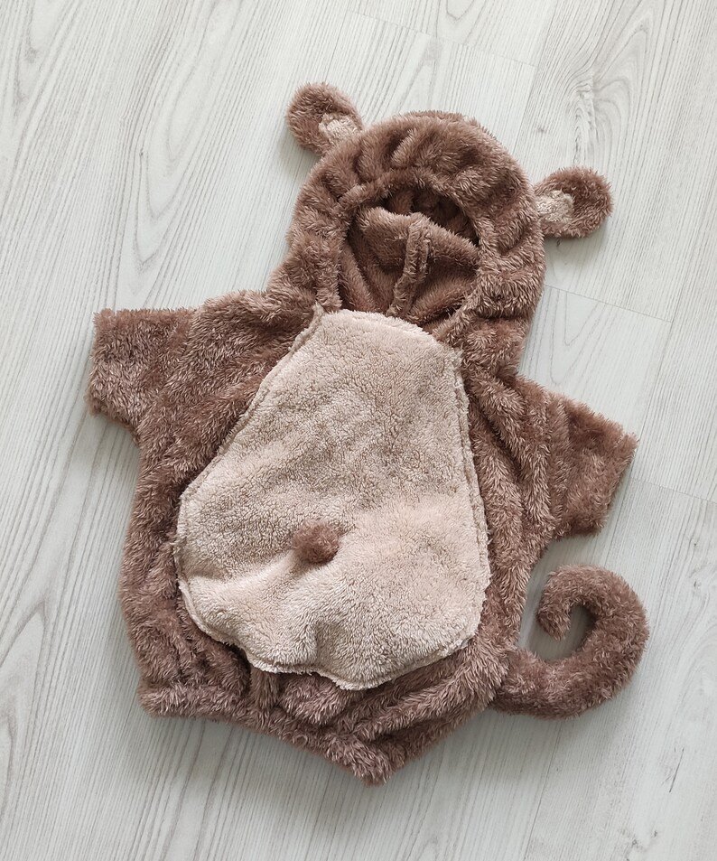 Puede incluir: Un disfraz de mono de peluche marr&oacute;n para un beb&eacute; o un ni&ntilde;o peque&ntilde;o. El disfraz tiene una capucha con orejas, una cola y un parche en el vientre.