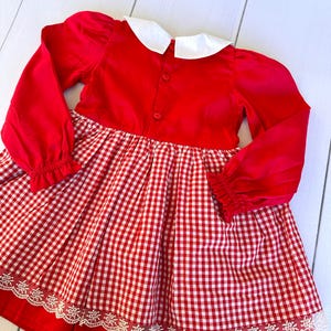 K&ouml;nnte beinhalten: Rot-wei&szlig;es Gingham-Kleid mit wei&szlig;em Peter-Pan-Kragen und langen &Auml;rmeln. Das Kleid hat einen Spitzenbesatz am Saum.