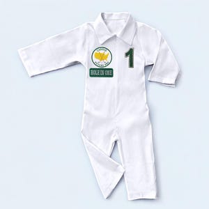 A vertical full-length photo of the white cotton golf caddy coverall. From the hem of the pants to the top of the collar, this shot demonstrates the proportions and fit of the outfit. The contrasting green graphics against the crisp white fabric create a classic, sporty look inspired by traditional golf tournament caddy gear.