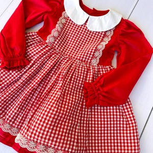 K&ouml;nnte beinhalten: Rot-wei&szlig;es Gingham-Kleid mit wei&szlig;er Spitzenborte und einem wei&szlig;en Peter-Pan-Kragen.