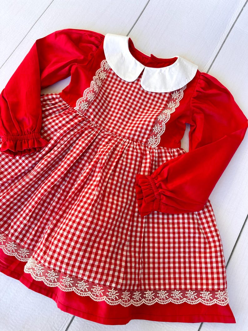 K&ouml;nnte beinhalten: Rot-wei&szlig;es Gingham-Kleid mit wei&szlig;er Spitzenborte und einem wei&szlig;en Peter-Pan-Kragen.