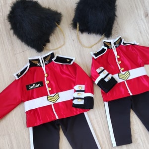 May include: Two red and black children's costumes with gold accents. The costumes feature a black fur hat, a red jacket with gold buttons and trim, and black pants with white trim. One costume has the name "Julian" on the jacket.