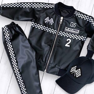 Peut inclure: Veste de course en cuir noir avec des rayures à carreaux blancs, pantalon assorti et casquette de baseball noire avec un motif de drapeau à damier. La veste a une fermeture éclair et le texte "G5 RACING 2" sur le devant.
