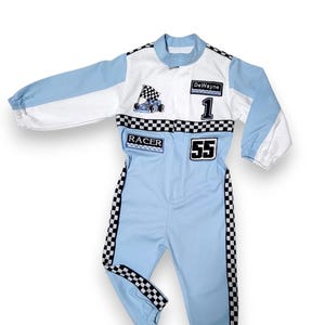 May include: A light blue racing suit with white and black checkered accents. The suit has a patch with a cartoon race car and the word "RACER" on it. The suit also has a patch with the name "DeWayne" and the number "1" on it. The suit has the number "55" on the leg.