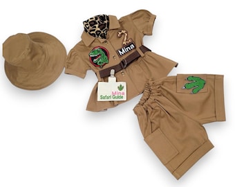 Puede incluir: Un disfraz de safari marrón para un niño, que incluye una camisa con un parche de dinosaurio, un cinturón, un sombrero, pantalones cortos con un parche de huella de dinosaurio y una etiqueta de nombre que dice "Mina Safari Guide".