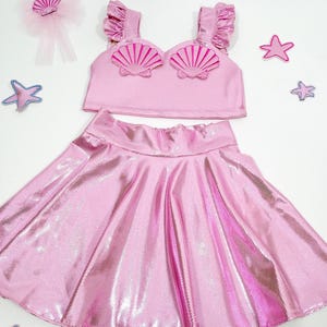 May include: A pink mermaid costume for girls, featuring a sparkly skirt and a crop top with pink seashell embellishments.