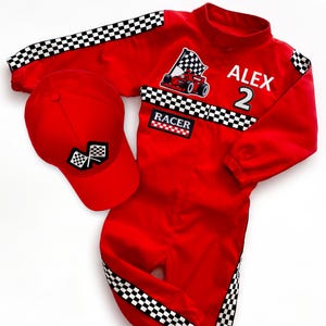 May include: A red racing-themed jumpsuit and matching baseball cap. The jumpsuit features black and white checkered stripes, a race car graphic, the name ALEX, the number 2, and a RACER patch. The cap displays a checkered flag emblem.