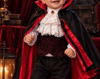 May include: A vampire costume featuring a black cape with a red lining, a white shirt with a ruffled lace collar and a red gemstone brooch, a dark red patterned vest, and black trousers. The ensemble is completed with black dress shoes.
