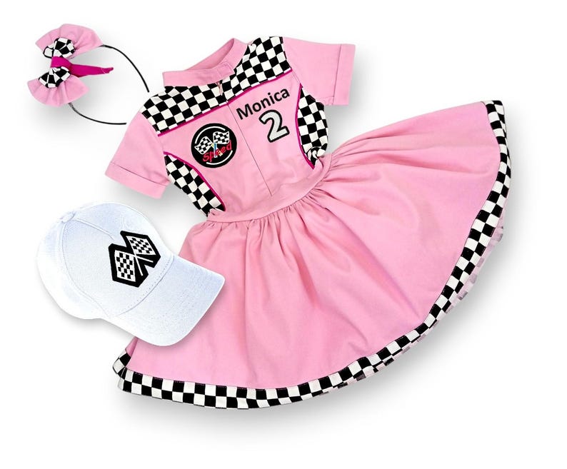 May include: Pink racing-themed dress with black and white checkered trim, a white cap with a checkered flag design, and a black headband with a pink bow. The dress has the name "Monica" and the number "2" on the front.
