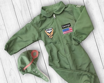 May include: Green pilot jumpsuit with a zipper closure, an American flag patch, and an Air Force patch. The jumpsuit has a name tag that says "George". A green pilot hat with a red trim and the name "George" is also included.