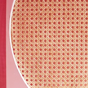 Peut inclure: Gros plan sur un motif en rotin tressé de couleur beige clair, sur fond rouge doux. Le rotin est disposé selon un motif géométrique répétitif, avec une bordure blanche incurvée et une section rouge unie à gauche.