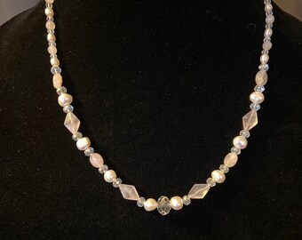 Pode incluir: Um colar delicado feito com contas cor-de-rosa e transparentes. O colar é feito com pequenas pérolas redondas e contas de cristal facetadas.