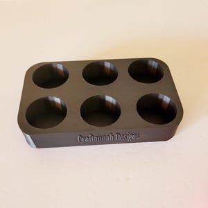 May include: A black plastic tray with six round depressions, designed to hold small items. The tray has the text "Craftannah Designs" printed on the bottom.