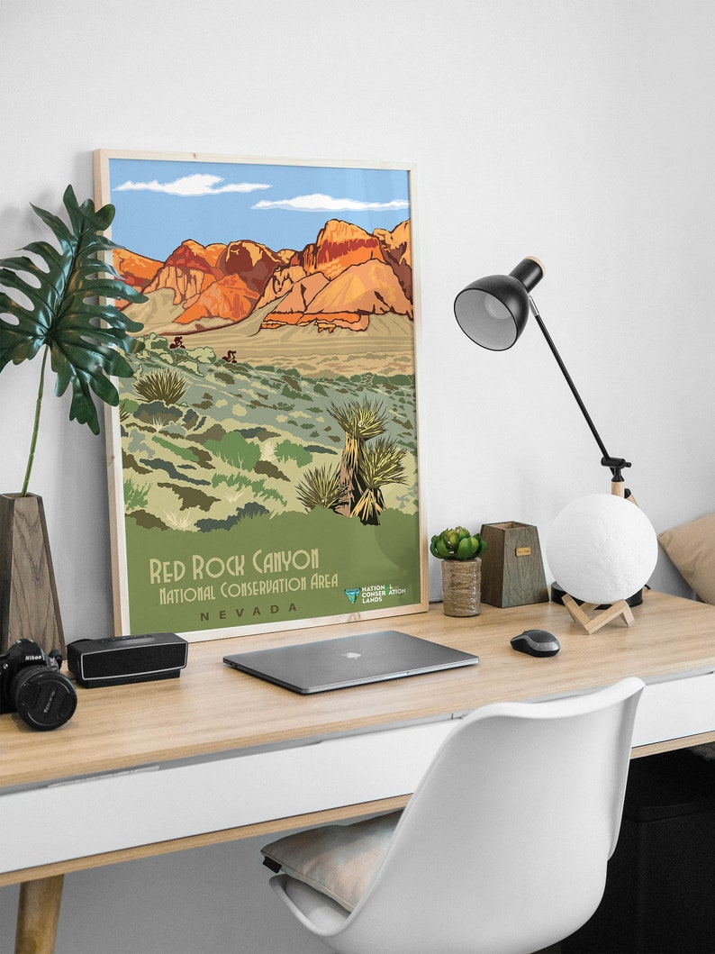 K&ouml;nnte beinhalten: Ein Vintage-Poster mit einer malerischen Illustration des Red Rock Canyon National Conservation Area in Nevada. Das Poster zeigt eine Bergkette mit roten Felsformationen und eine W&uuml;stenlandschaft mit gr&uuml;ner Vegetation. Der Text "Red Rock Canyon National Conservation Area Nevada" ist am unteren Rand des Posters gedruckt.