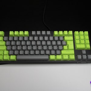 Könnte beinhalten: Eine mechanische Tastatur mit schwarzem Rahmen und einer Mischung aus grauen und limettengrünen Tastenkappen. Die Tastatur hat ein Standardlayout mit Nummernblock und Funktionstasten. Das Bild ist vor einem schwarz-weißen Hintergrund.