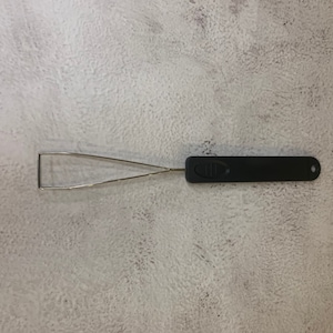 Könnte beinhalten: Ein schwarzes Keycap-Abziehwerkzeug mit einem rechteckigen Griff und einer Drahtschlaufe. Das Werkzeug dient zum Entfernen von Tastenkappen von Tastaturen. Der Griff hat ein strukturiertes Design für den Halt und ein kleines Loch am Ende.