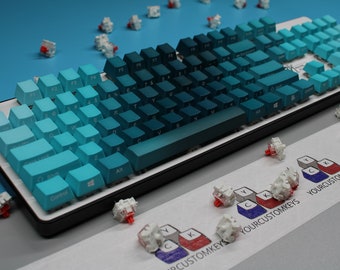 May include: A mechanical keyboard with a blue gradient keycap design. The keycaps transition from light to dark blue. Several loose key switches are scattered around the keyboard. The text "YOURCUSTOMKEYS" is visible.