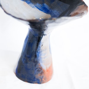 Peut inclure: Un vase en céramique avec une large ouverture évasée et une base étroite. Le vase est peint dans des tons de bleu, blanc et marron, créant un effet marbré.