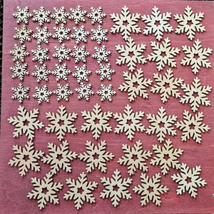 May include: A collection of wooden snowflake cutouts in various sizes. The snowflakes are arranged on a reddish-brown surface. Each snowflake has intricate details, with multiple points and a central star-shaped design. Ideal for holiday crafts and decorations.