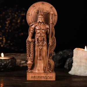 Pode incluir: Estátua de madeira de uma figura com coroa, segurando um bastão e uma corrente, com a palavra "BELHEGOR" na base. A estátua está em um fundo escuro com velas acesas e elementos decorativos.