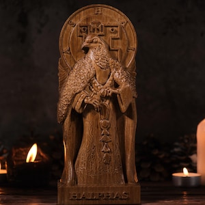 May include: A detailed wooden statue of a bird-like figure with outstretched wings, wearing a robe and holding a staff. The statue is carved with intricate details and stands on a base with the name "HALPHAS".