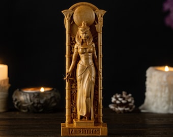 Puede incluir: Estatua de madera de Neftis, diosa egipcia, con tallado detallado, incluyendo tocado y vestido. El nombre "NEPHTHYS" está grabado en la base. Velas encendidas y piñas en el fondo.