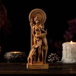 May include: Wooden statue of the Roman goddess Diana, depicted with a deer and a dog. The statue is on a wooden base with the word "Diana" inscribed on it. The statue is surrounded by candles and pine cones.