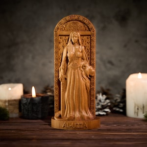May include: A wooden carving of a female figure holding a sword and a lion. The carving is in a decorative frame and has the text "AL-UZZA" at the bottom.