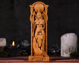 Puede incluir: Estatua de madera de Maat, la diosa egipcia de la verdad, la justicia y el orden cósmico. La estatua está tallada en madera clara y presenta detalles intrincados, incluyendo alas, una tocado y balanzas. La palabra "MAAT" está tallada en la base.