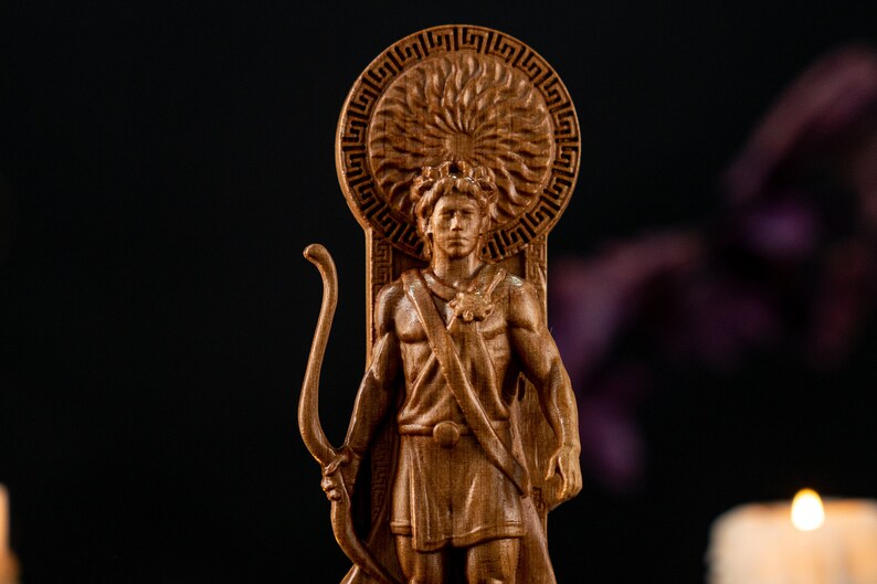 Może przedstawiać: Drewniana statua mężczyzny z łukiem i strzałą, być może postać mitologiczna. Statua jest wyrzeźbiona w drewnie i ma skomplikowane detale, w tym wz&oacute;r promieni słonecznych za głową postaci. Statua jest brązowa i stoi na ciemnym tle.