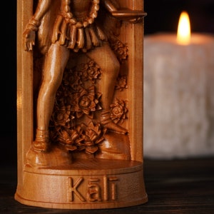 Pu&ograve; includere: Scultura in legno dettagliata della dea ind&ugrave; Kali. La scultura presenta intricati dettagli della sua forma e del suo abbigliamento. Lo sfondo sfocato mette in risalto i toni caldi del legno e il tema spirituale.