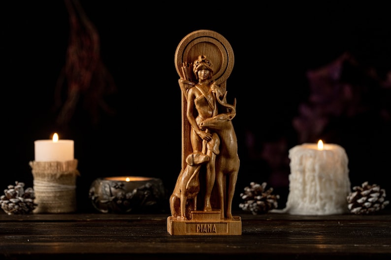 May include: Wooden statue of the Roman goddess Diana, depicted with a deer and a dog. The statue is on a wooden base with the word "Diana" inscribed on it. The statue is surrounded by candles and pine cones.