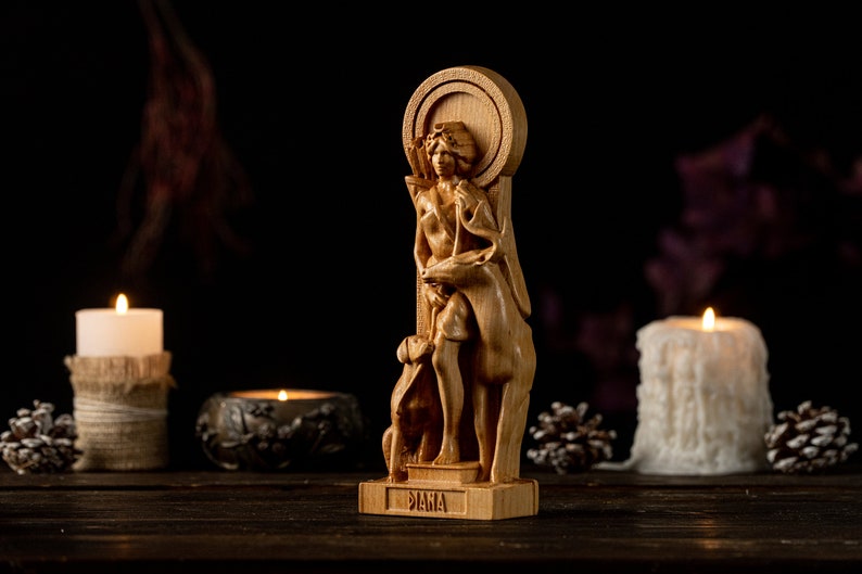 May include: A wooden statue of the Roman goddess Diana, depicted with a bow and arrow, standing with a deer and a dog. The statue is on a wooden base with the word "Diana" inscribed on it. The statue is surrounded by candles and pine cones.