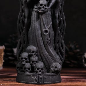 Puede incluir: Estatua negra de la Parca con base adornada con calaveras y una capa con capucha. La estatua presenta m&uacute;ltiples calaveras en la base y un colgante en forma de llave. Tema g&oacute;tico.