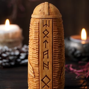 May include: A wooden box with a carved lid and runes on the front. The box is sitting on a dark wooden surface with two candles in the background.