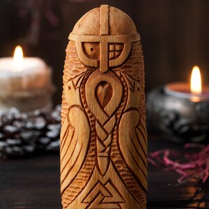 May include: A wooden carving of a Norse god, possibly Odin, with a beard, helmet, and wings. The carving is detailed with intricate patterns and symbols.