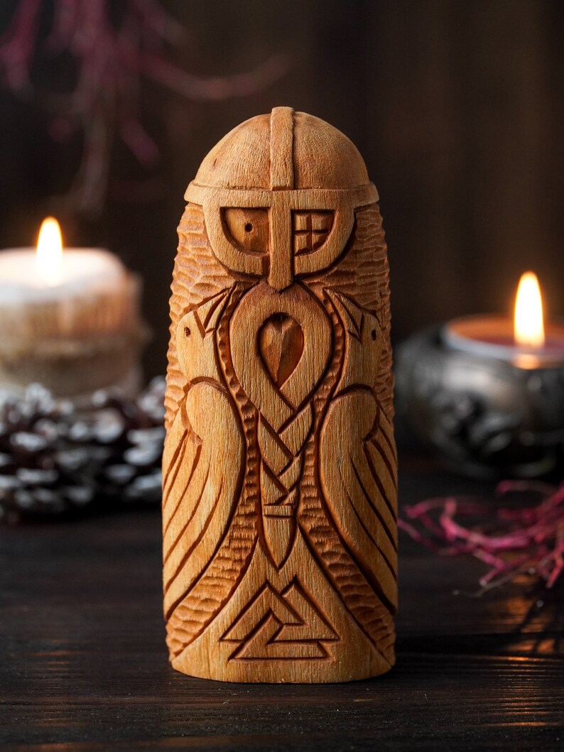 May include: A wooden carving of a Norse god, possibly Odin, with a beard, helmet, and wings. The carving is detailed with intricate patterns and symbols.
