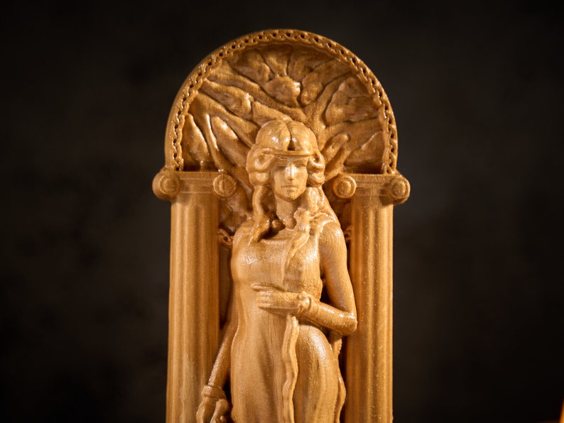 May include: A wooden sculpture of a woman in a flowing robe, standing in a doorway with a decorative archway. The sculpture is carved in a light brown wood and has a detailed design.