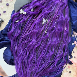 a close-up view of a person's long, vibrant purple hair with various hair accessories, such as small silver charms, placed throughout the hair.