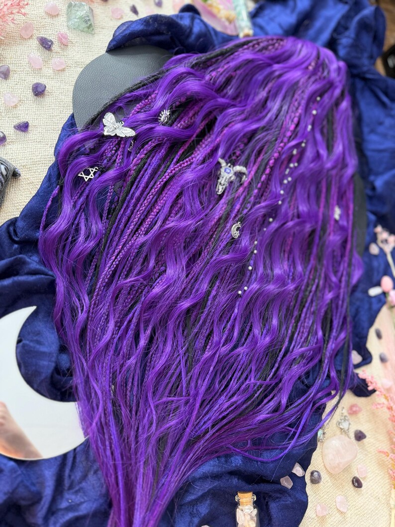 a close-up view of a person's long, vibrant purple hair with various hair accessories, such as small silver charms, placed throughout the hair.