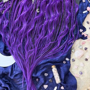 a close-up view of a person's long, vibrant purple hair, adorned with various accessories such as crystals and jewelry.