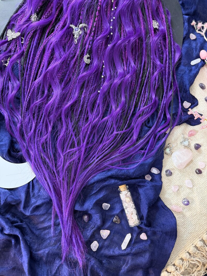 a close-up view of a person's long, vibrant purple hair, adorned with various accessories such as crystals and jewelry.