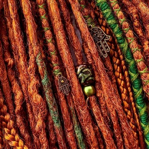 a close-up view of a collection of braided hair strands in various colors, including orange, green, and brown, with some beads and charms attached.